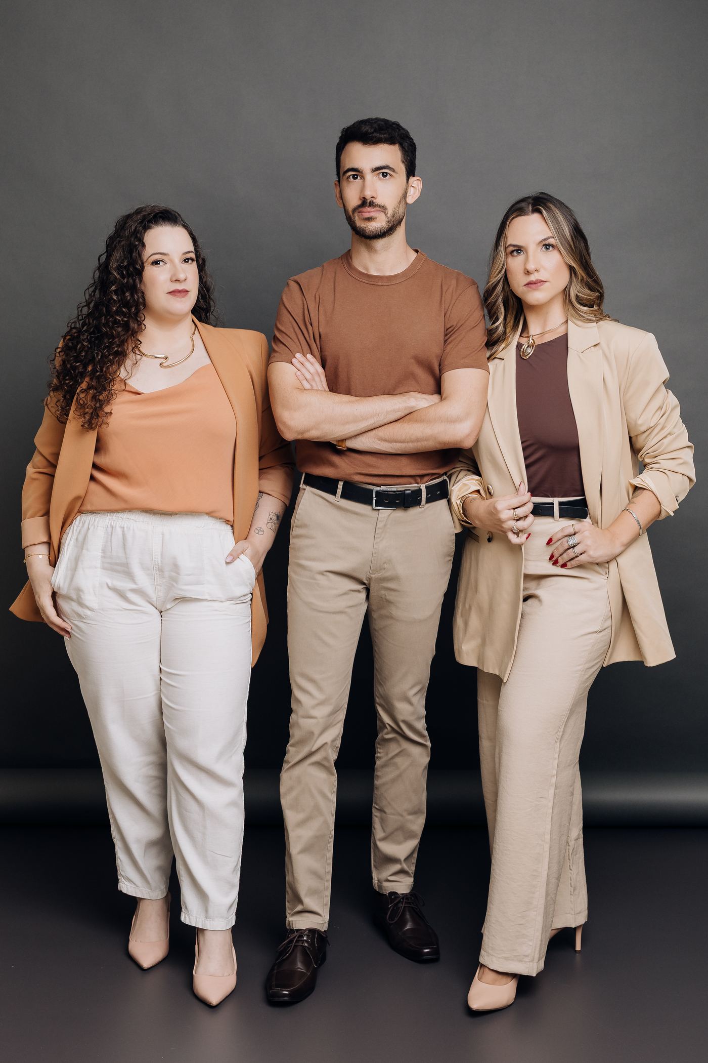 Carla, Bruno e Carolina, a equipe da Athom, em pé lado a lado num estúdio de fundo cinza