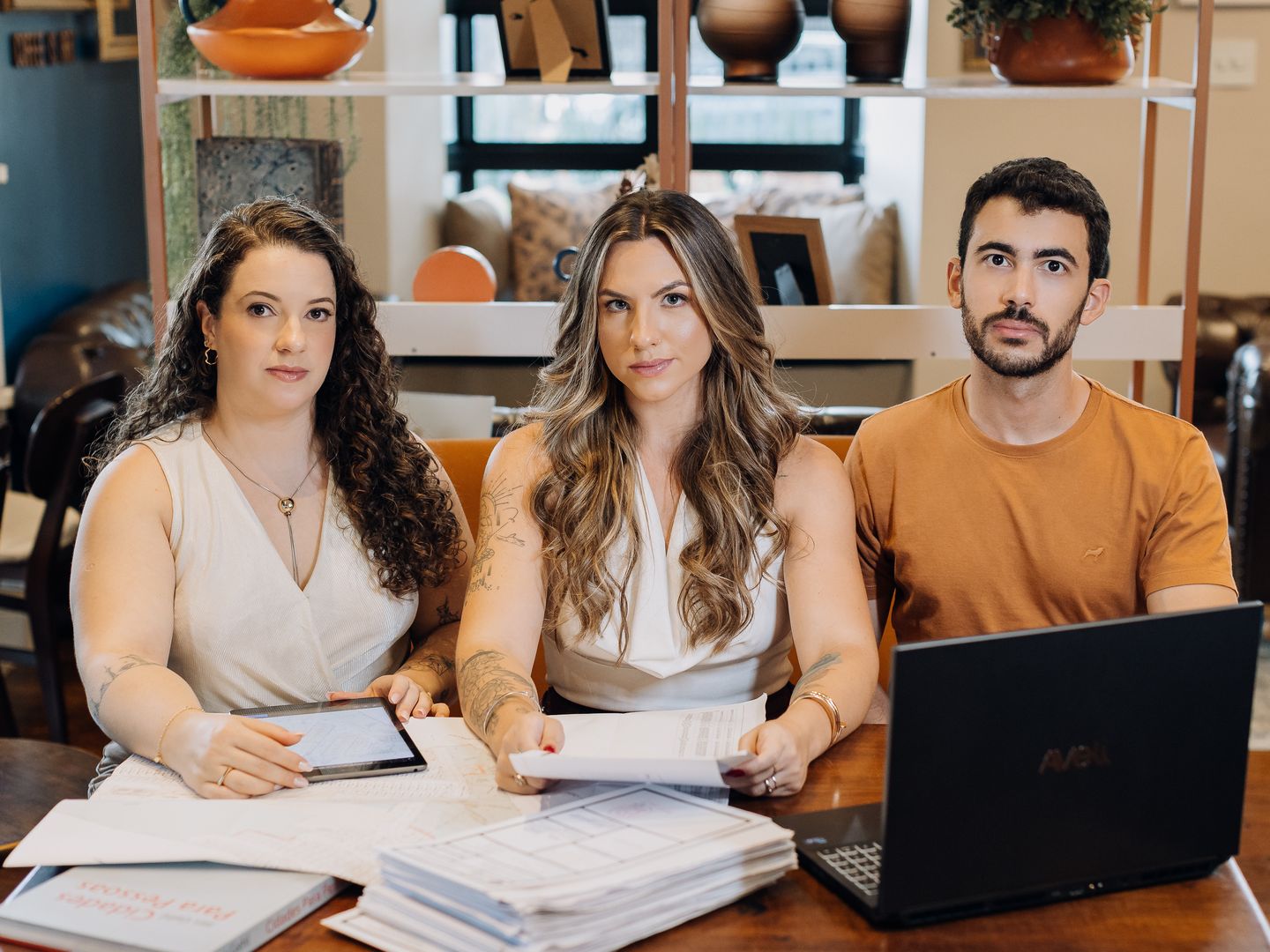 Bruno, Carla e Carolina, equipe da Athom, sentados à mesa de trabalho com plantas de loteamento, tablet e notebook